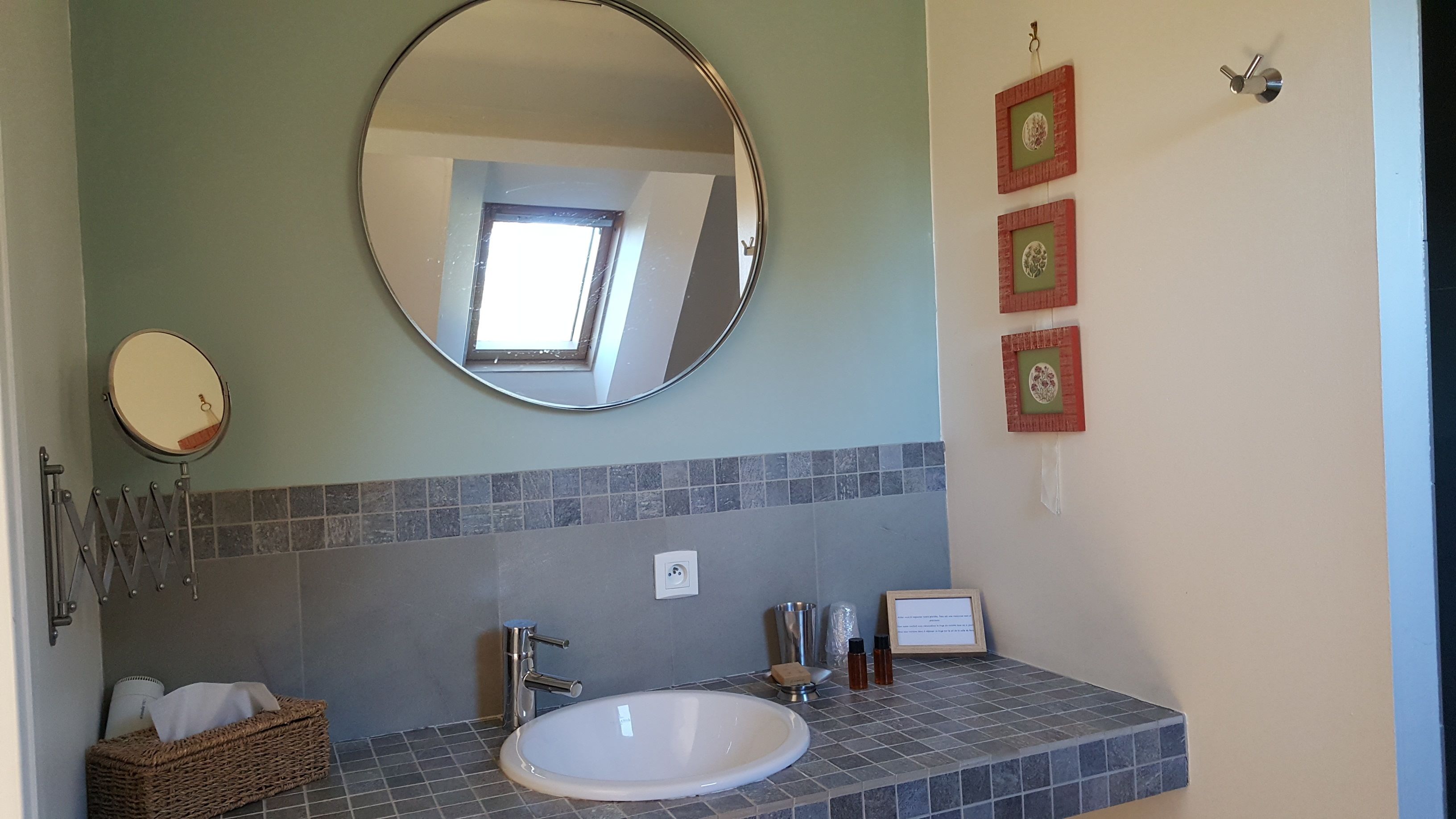 Ein Badezimmer mit rundem Spiegel, Waschbecken, Handtuchhalter und kleinem Fenster.