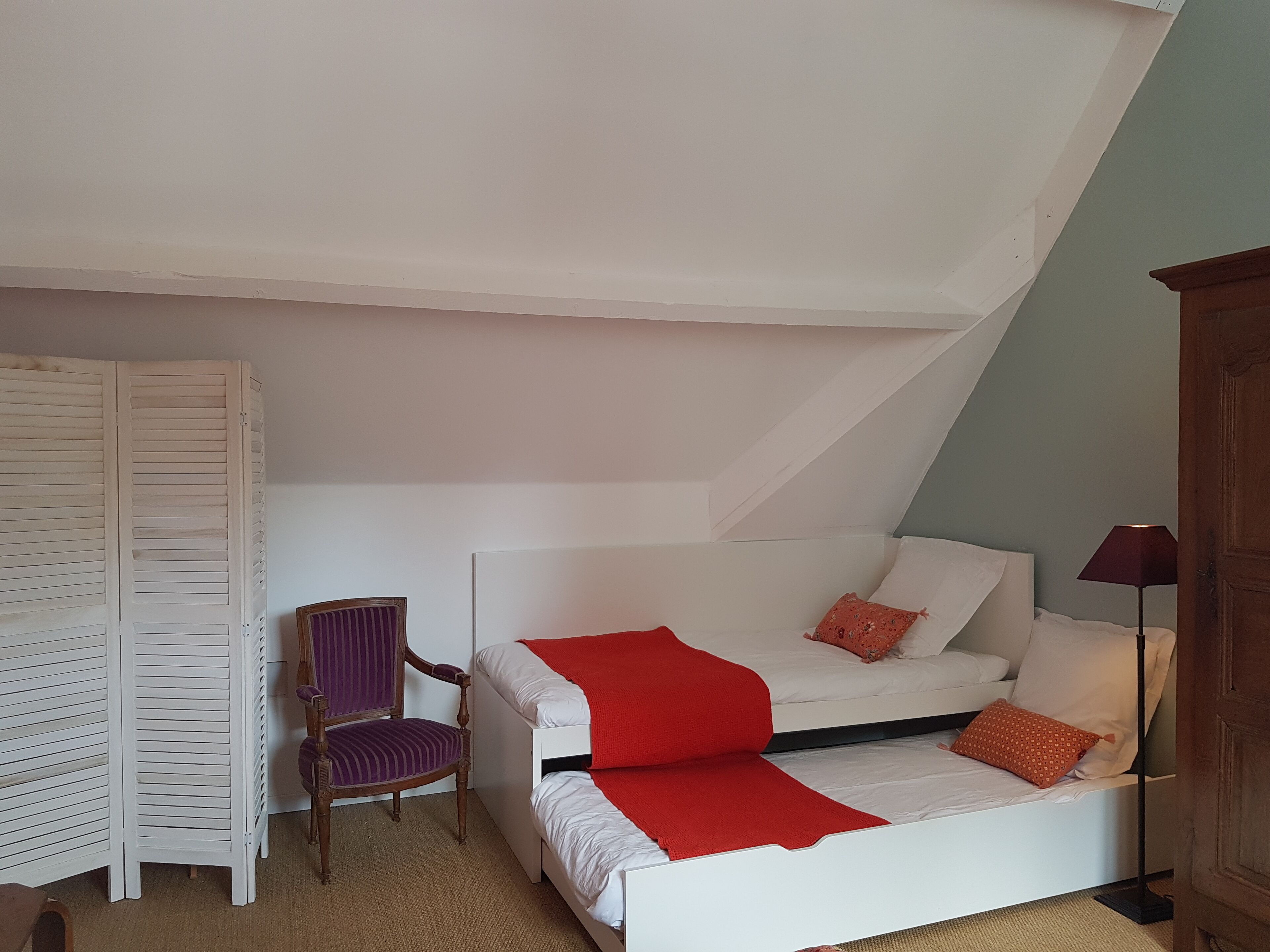 Una camera da letto con un letto bianco, una coperta rossa e una sedia viola.