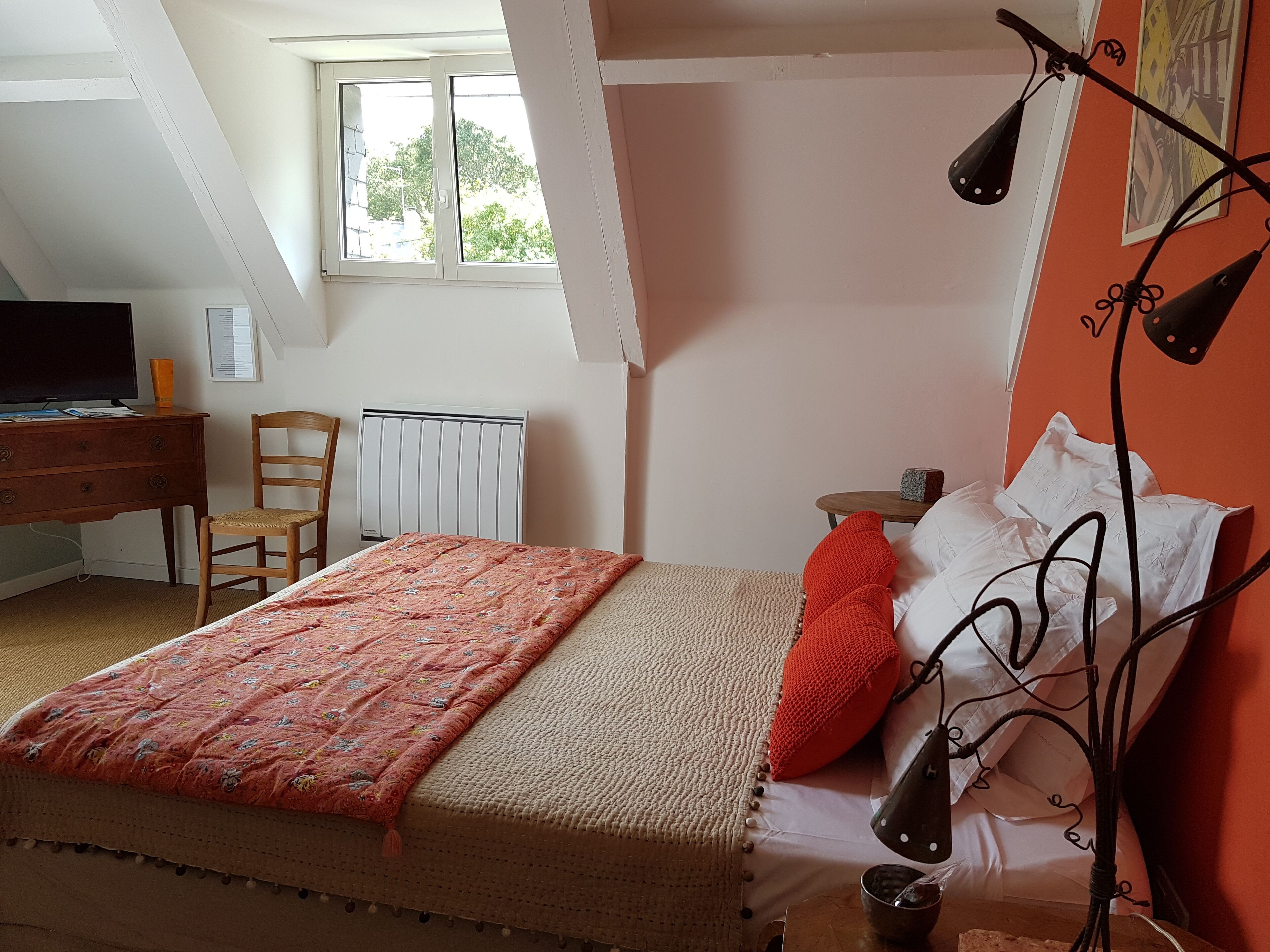 A bedroom with a bed, a desk, a chair, a radiator, and a window.