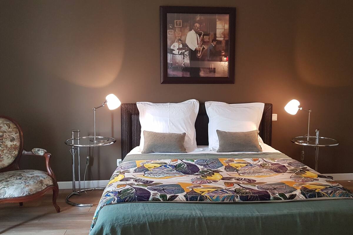 A bedroom with a bed, two bedside lamps, a chair, and a framed picture on the wall.