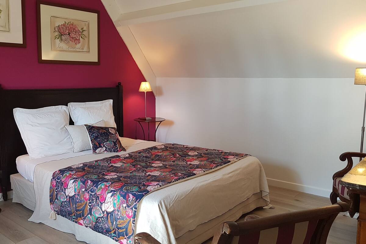 A bedroom with a bed, two bedside tables, a nightstand, a chair, and a red accent wall.