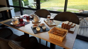 A breakfast table set with tea cups, a teapot, jam, bread, and small dishes of butter and jam.