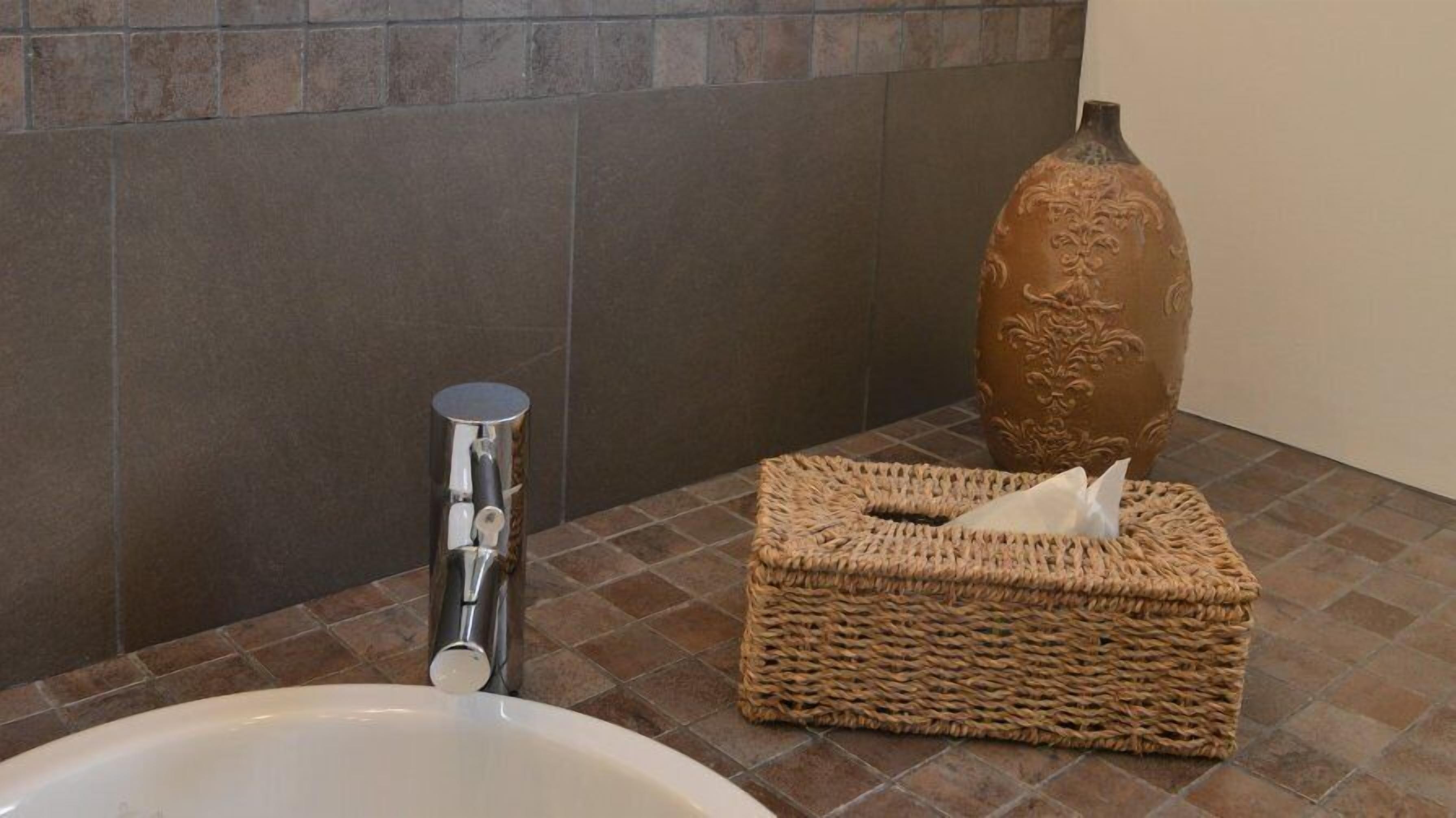 Ein Badezimmer mit einer weißen Badewanne, einem Metall-Handtuchspender, einem gewebten Korb mit Taschentüchern und einer dekorativen Vase.