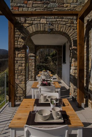 Un espacio de comedor al aire libre con paredes de piedra y vigas de madera, con mesas y sillas dispuestas para comer.