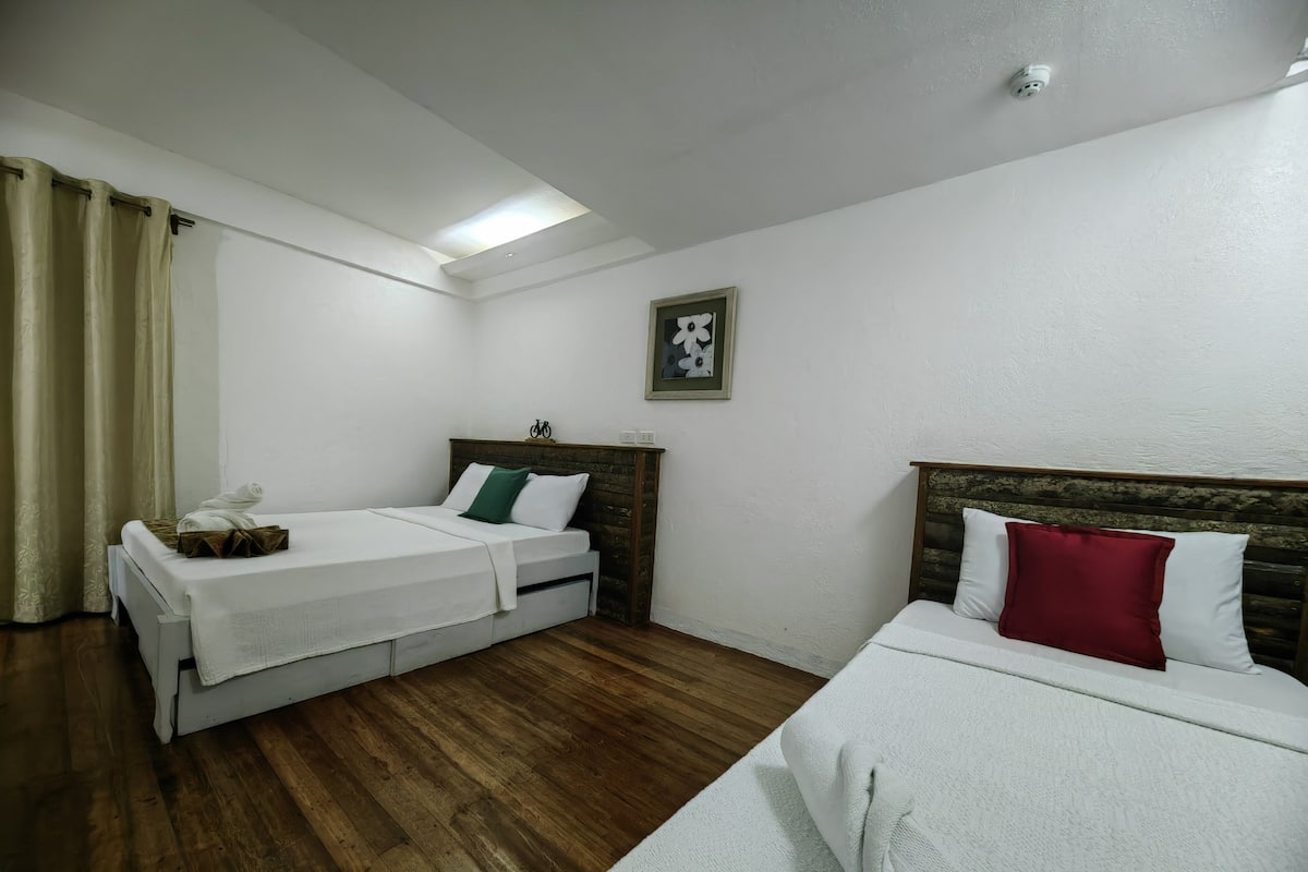 Une chambre d’hôtel avec deux lits, un plancher en bois, des murs blancs, un luminaire au plafond et une caméra de surveillance.
