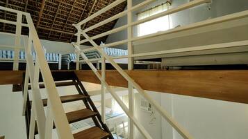 A staircase with wooden steps and white railings leading to a room with a thatched roof ceiling and a bed with a striped blanket.