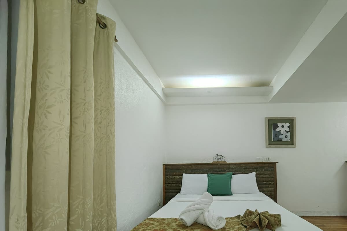 Un lit simple avec une tête de lit blanche, un oreiller vert et une serviette blanche roulée posée sur le lit.