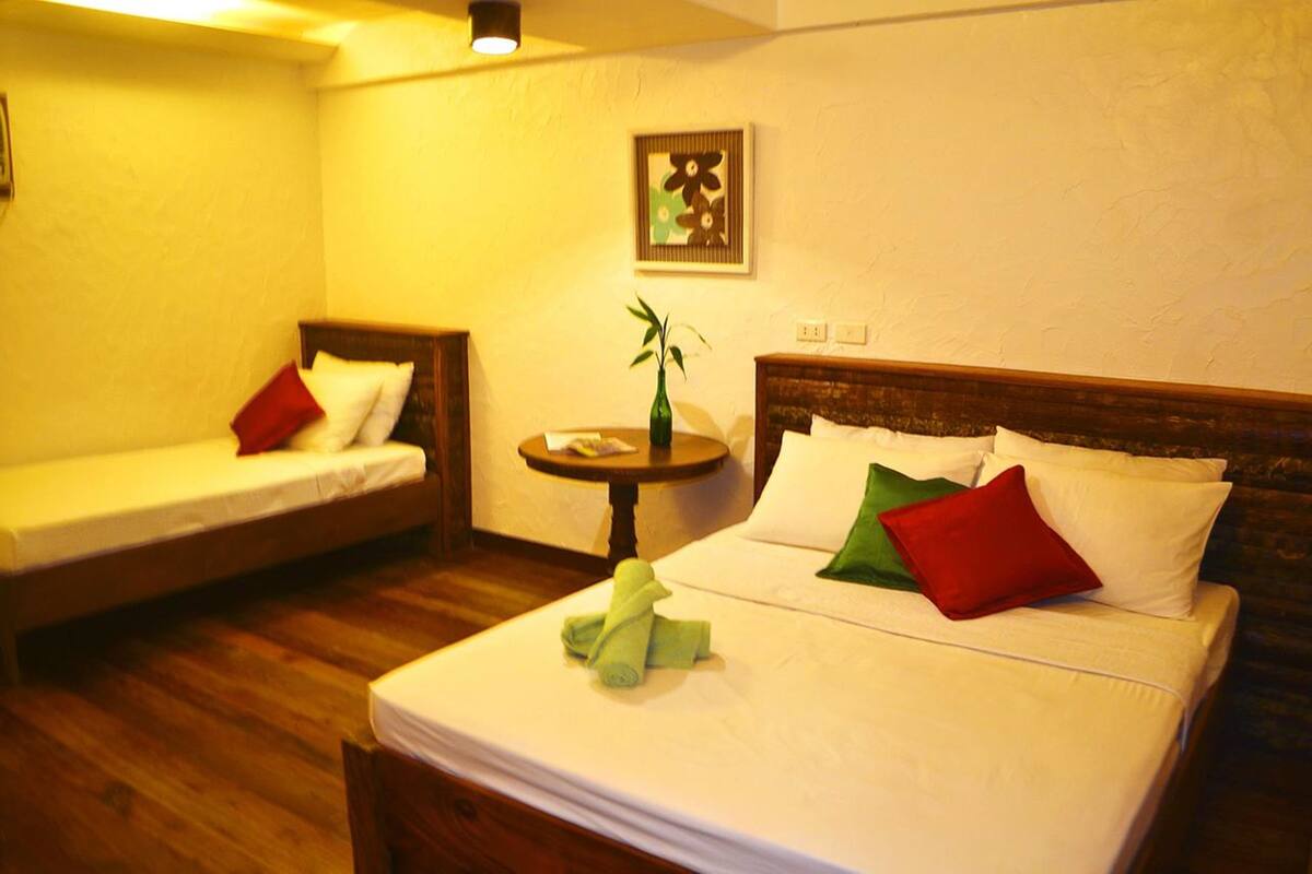 Une chambre d’hôtel avec un lit, un canapé, une petite table avec un vase et un tableau accroché au mur.