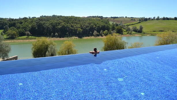 A person swimming in a large, clear blue pool with a view of a lake and hills in the background.