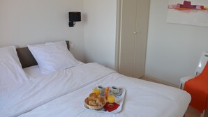 A neatly made bed with white linens, a tray with bread, juice, and coffee, and a wall-mounted lamp.