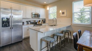 A modern kitchen with stainless steel appliances, a central island with bar stools, and a dining area with a wooden table and chairs.