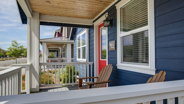 A porch with a wooden railing, a red door, and a bench.