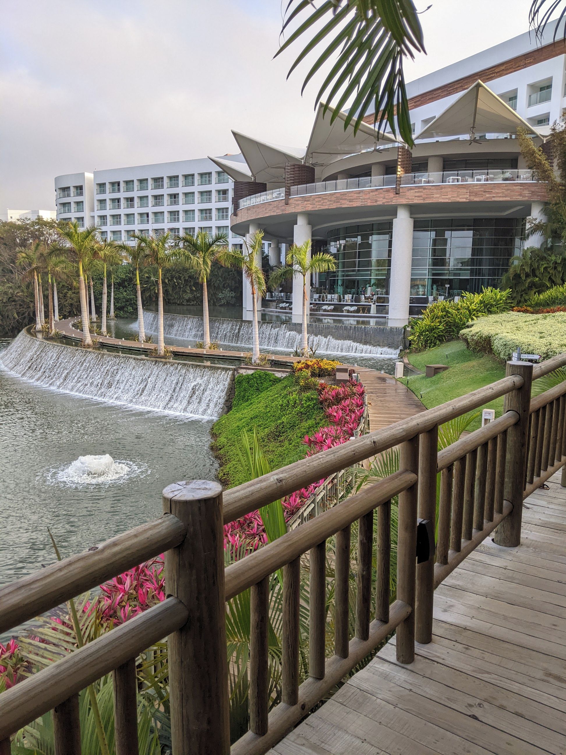 Een modern hotel met een waterval, een houten terras en weelderige beplanting.