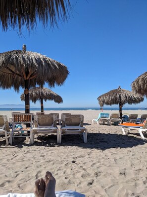 A beach with thatched umbrellas and lounge chairs.