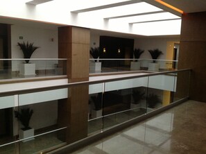 A modern interior with a glass railing, potted plants, and a high ceiling with skylights.