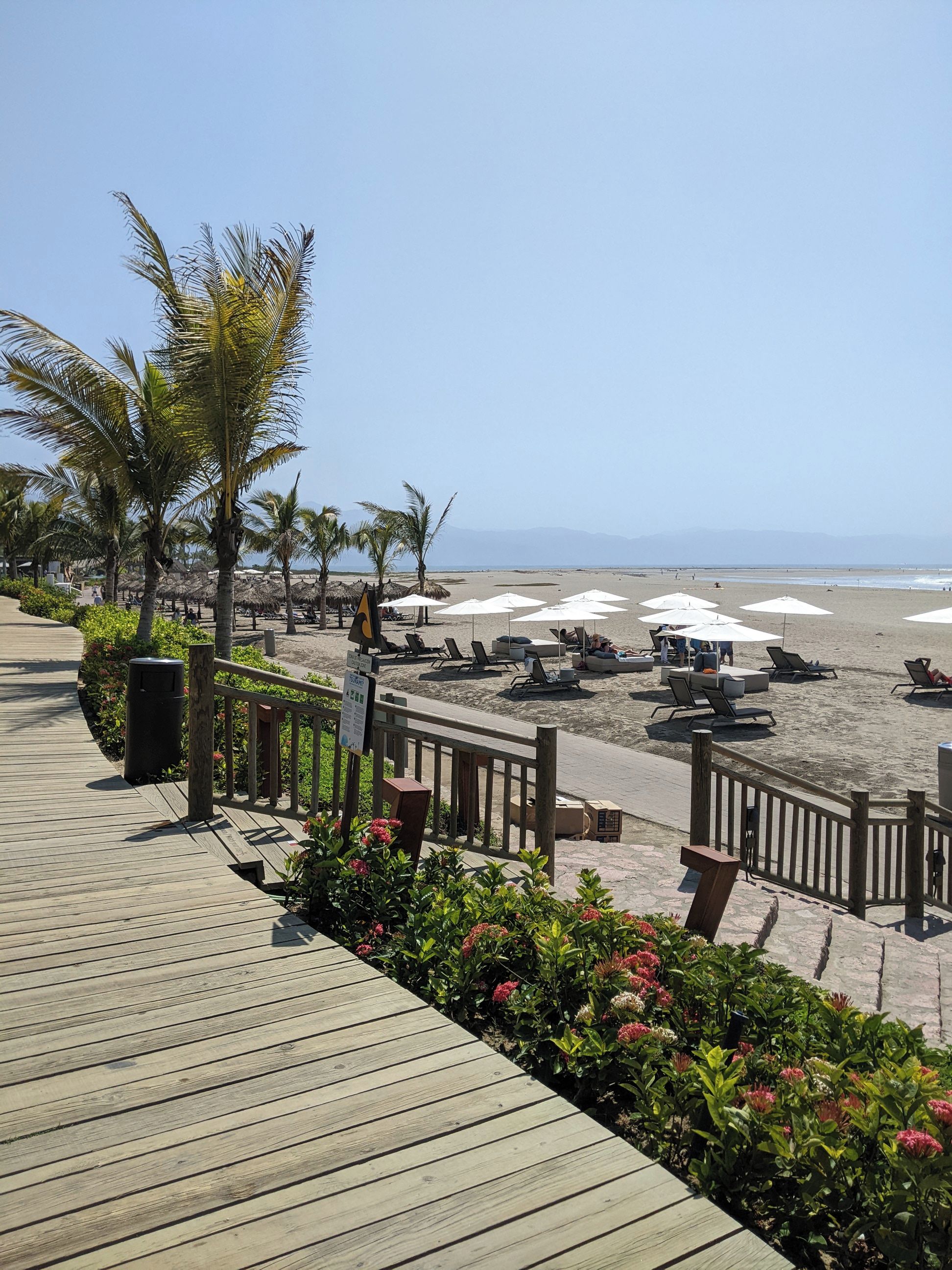 A wooden boardwalk leading to a beach with lounge chairs and umbrellas.