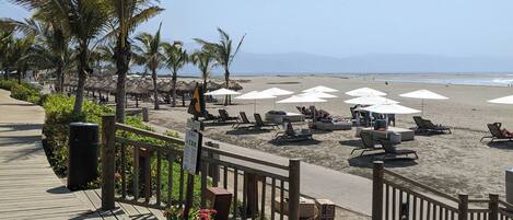 A wooden boardwalk leading to a beach with lounge chairs and umbrellas.
