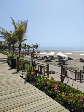 Une promenade en bois menant à une plage où se trouvent des chaises longues et des parasols.