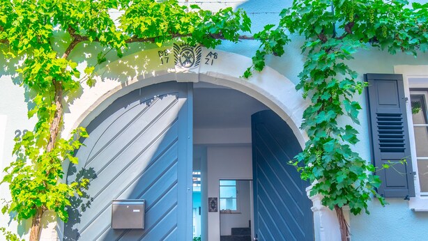 Um edifício com uma grande entrada em arco, uma escadaria que leva para dentro e uma varanda com vegetação.