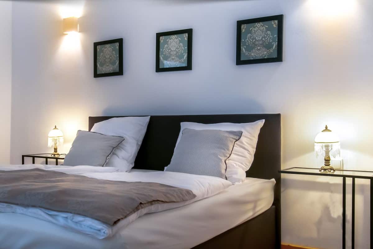 A neatly made bed with a gray blanket and white linens, flanked by two bedside tables with lamps.