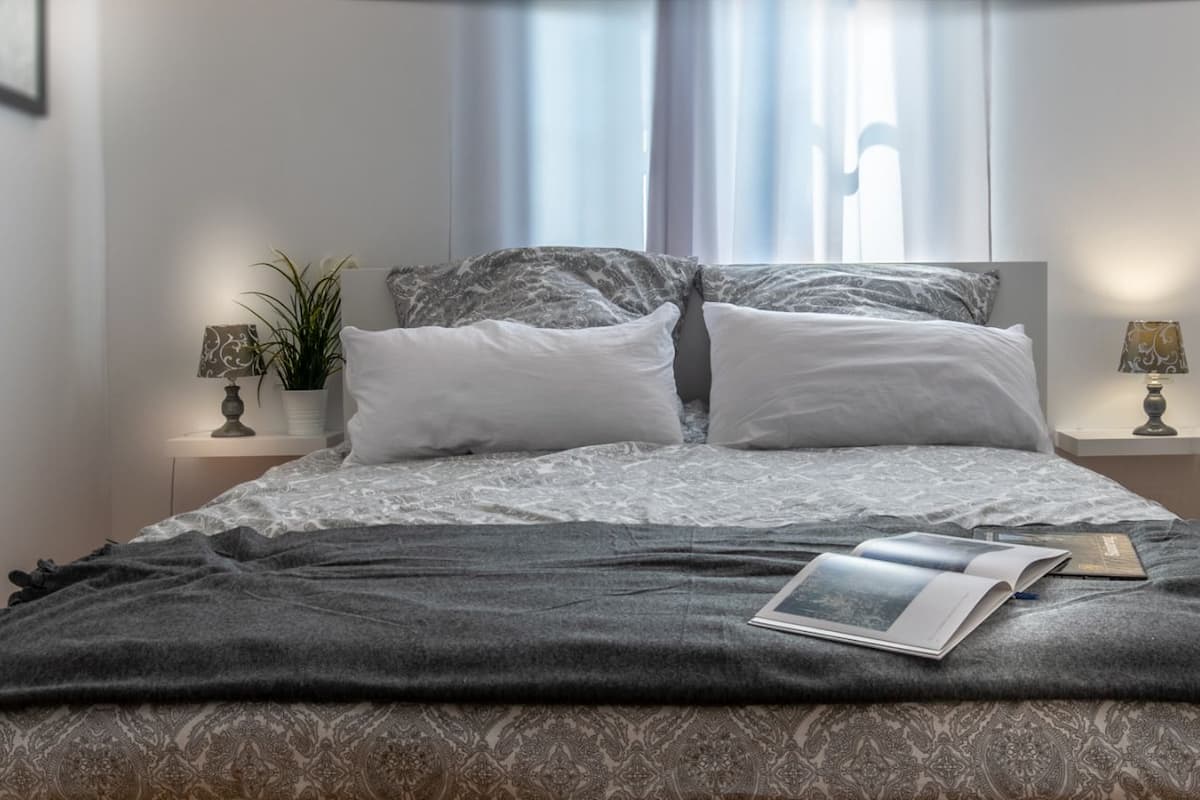 A neatly made bed with a patterned bedspread, two bedside lamps, and a book on the bed.