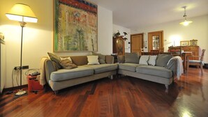 Ein Wohnzimmer mit Ecksofa, einem großen Gemälde, Holzboden und einer Essecke mit Tisch und Stühlen.