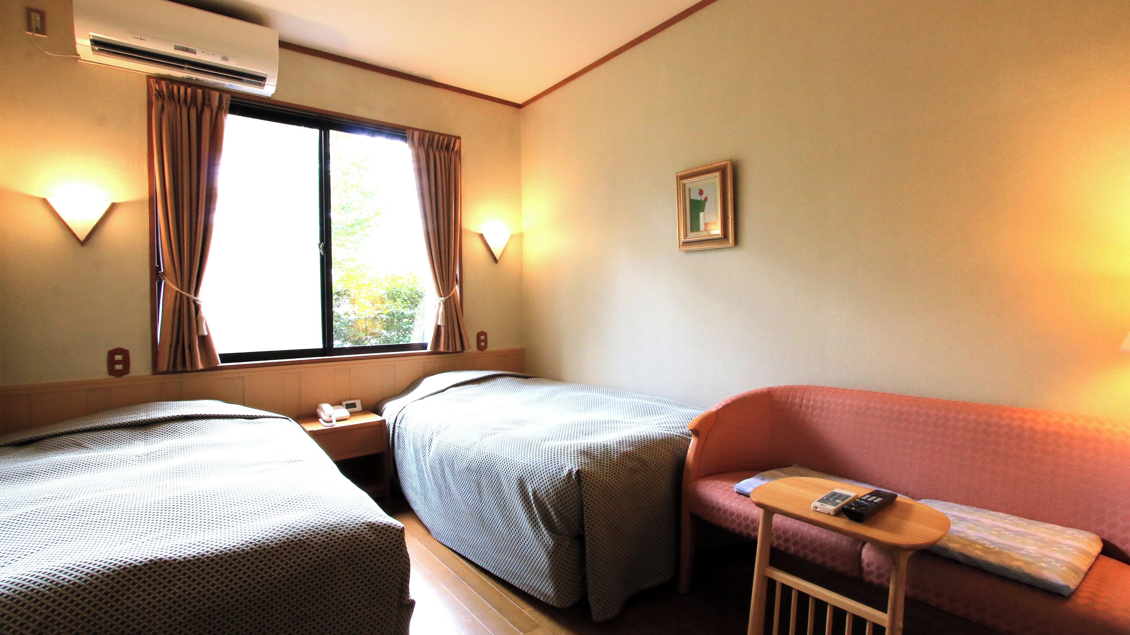A hotel room with two beds, a sofa, a small table, and a window with curtains.