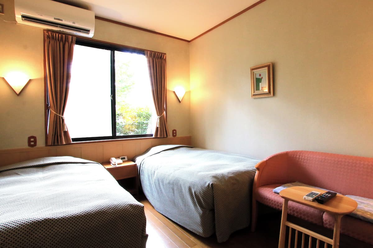 A hotel room with two beds, a sofa, a small table, and a window with curtains.