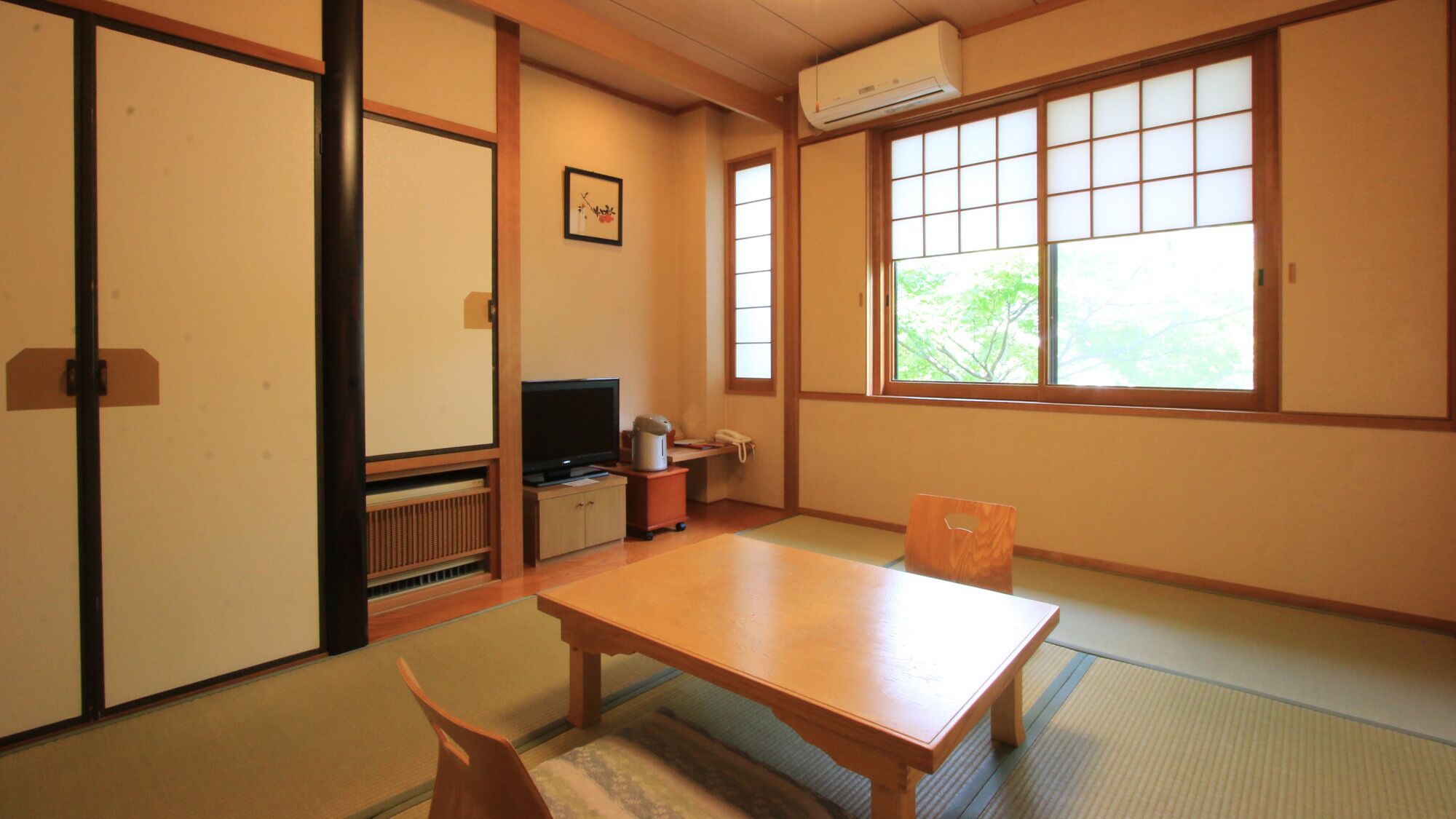 A traditional Japanese room with tatami flooring, a low table, a television, and sliding doors.
