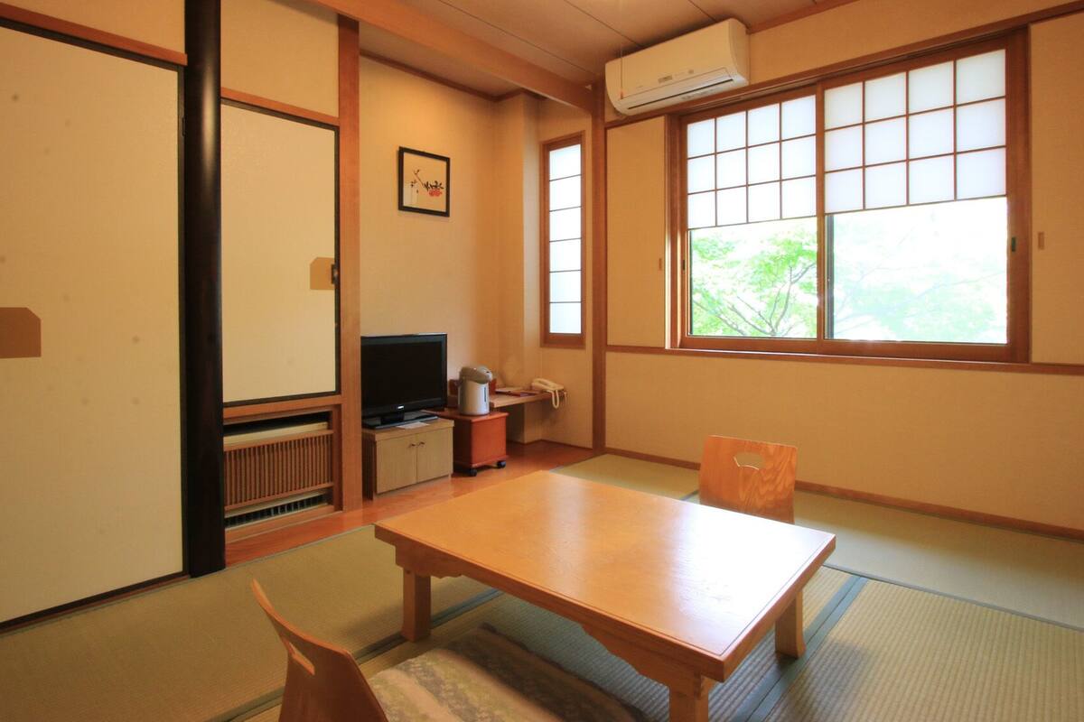 A traditional Japanese room with tatami flooring, a low table, a television, and sliding doors.