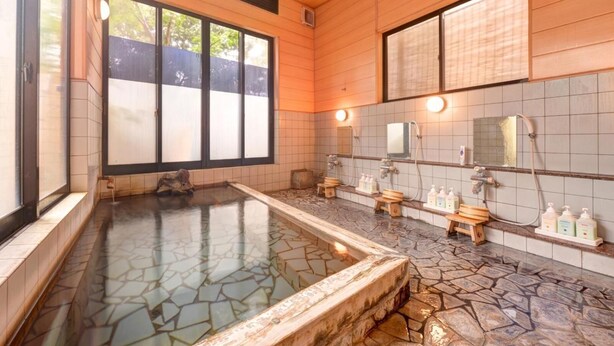 A traditional Japanese onsen with a stone hot spring, wooden benches, and a tiled wall with mirrors and toiletries. - Yufuin Yamaboushi (Yufu)