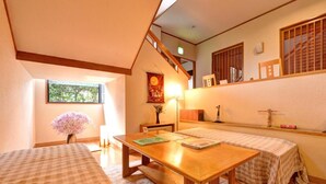 A cozy room with a wooden table, two beds, a window with a view, and a staircase. - Yufuin Yamaboushi (Yufu)