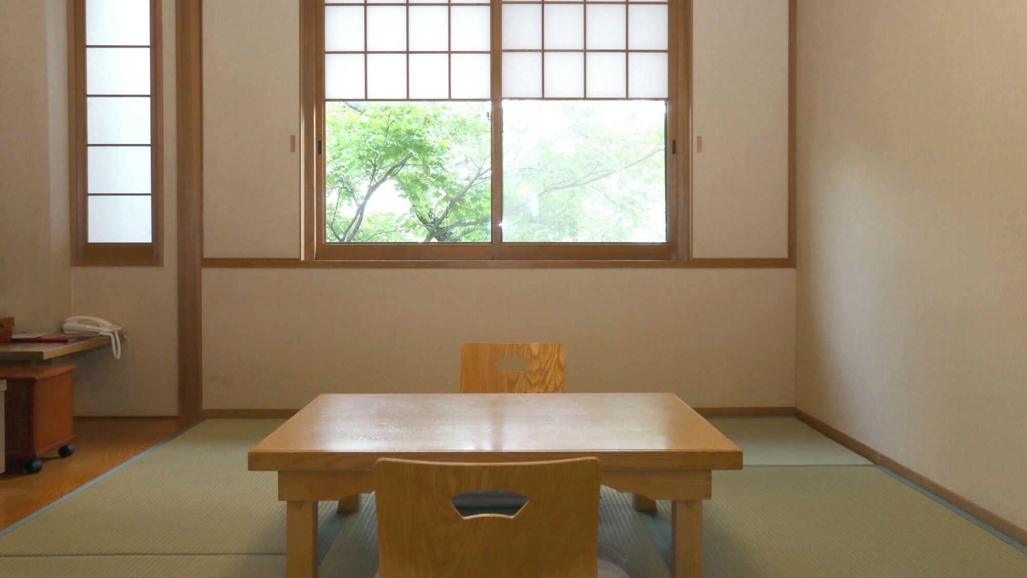 A room with tatami flooring, a wooden table, a chair, and a window with a view of trees.