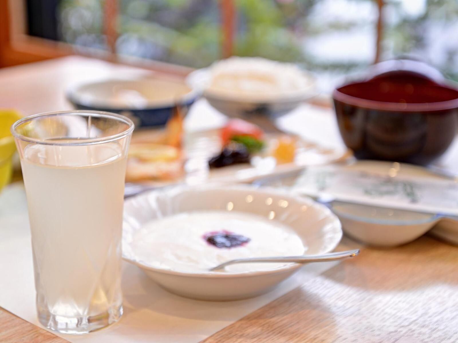 A dining table with a glass of milk, a bowl of yogurt with a berry, and various dishes in the background.