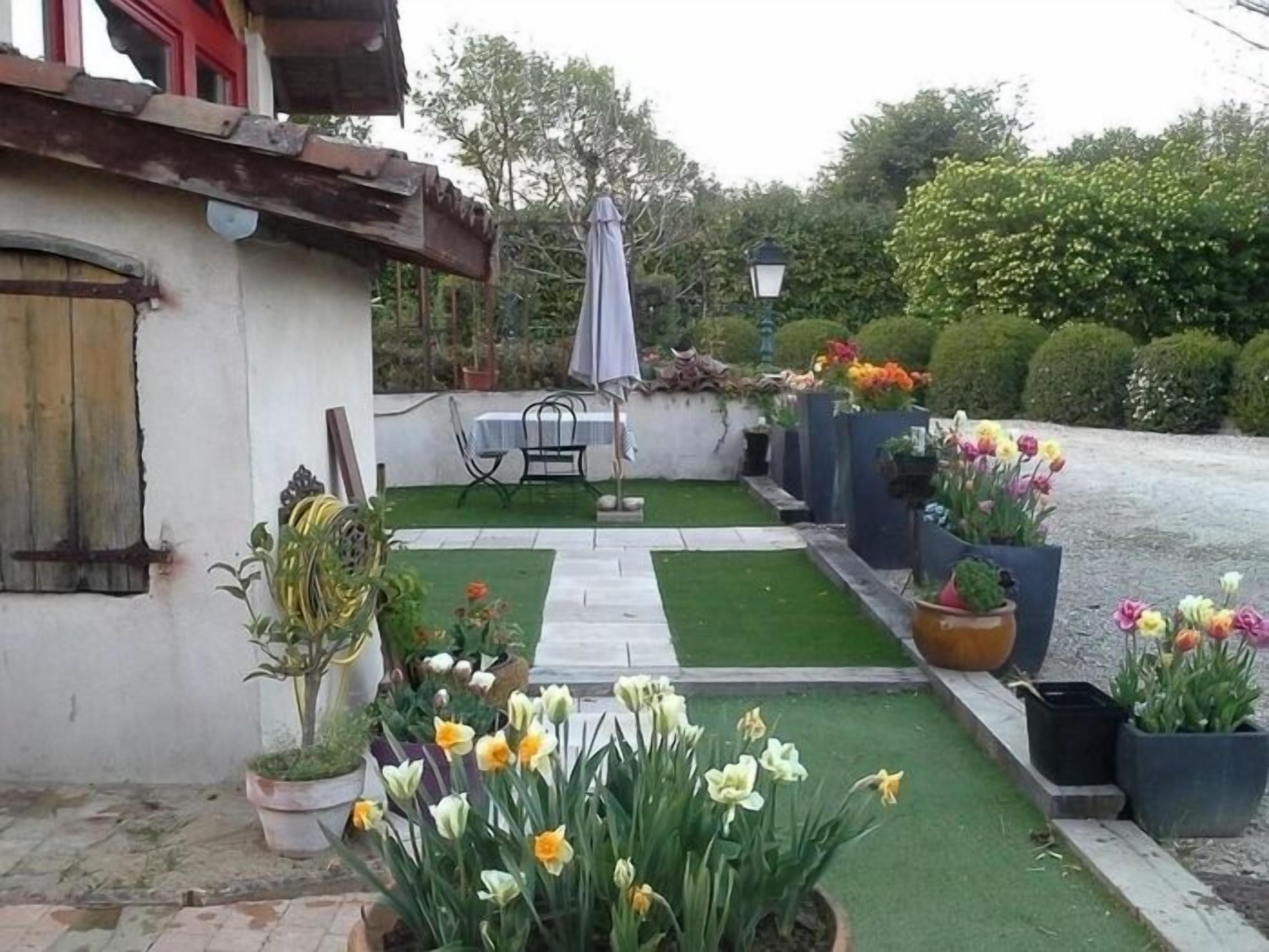 A small garden area with a table and chairs, potted plants, and a variety of flowers.
