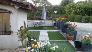 A small garden area with a table and chairs, potted plants, and a variety of flowers.