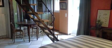 A bedroom with a bed, a staircase, a dining table, and chairs.