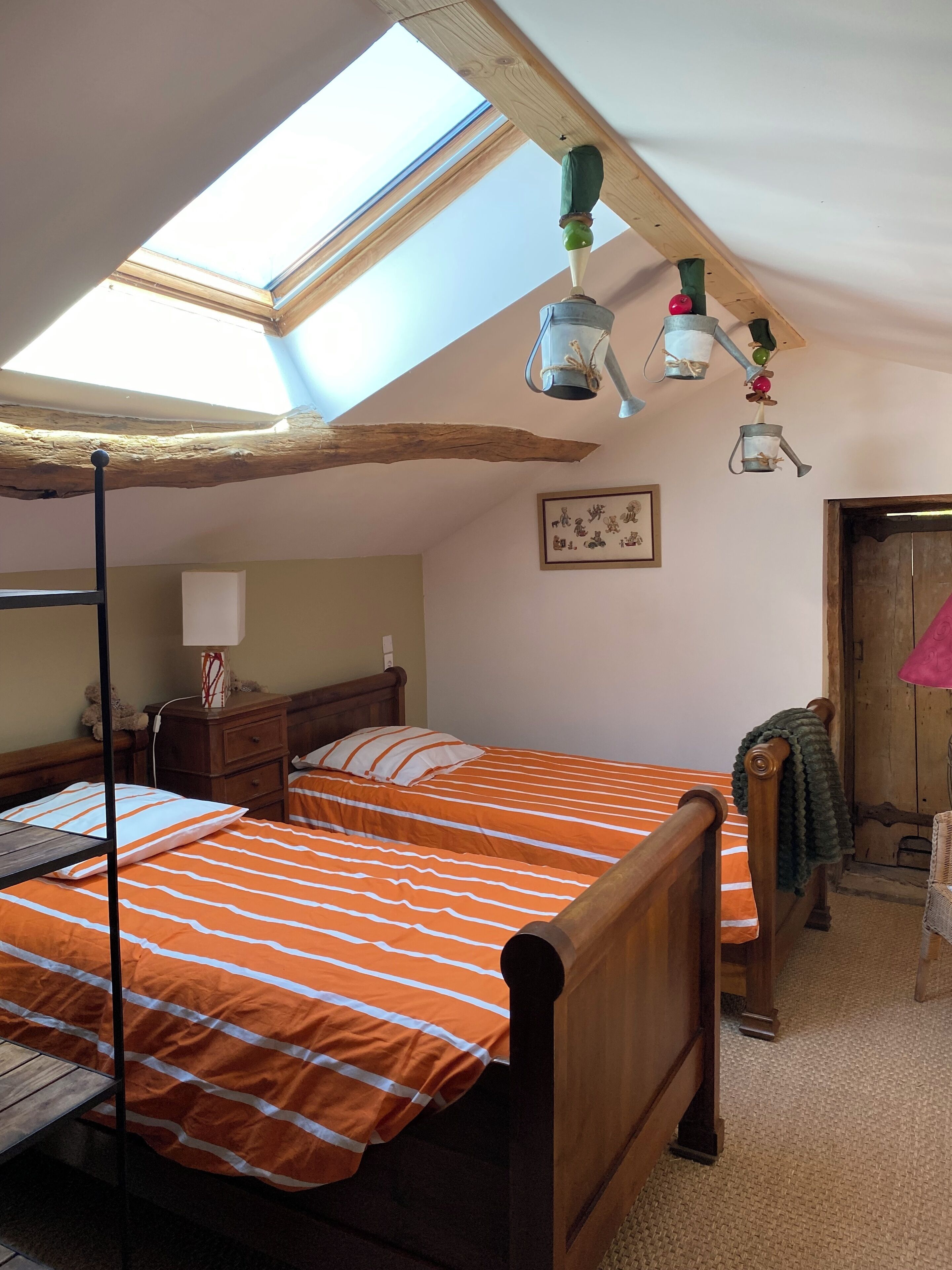 A bedroom with two beds, a skylight, wooden beams, a nightstand, a dresser, and a framed picture on the wall.