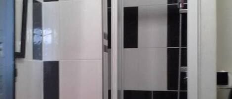 A bathroom with a glass shower enclosure, a red sink, and black and white tiled walls.