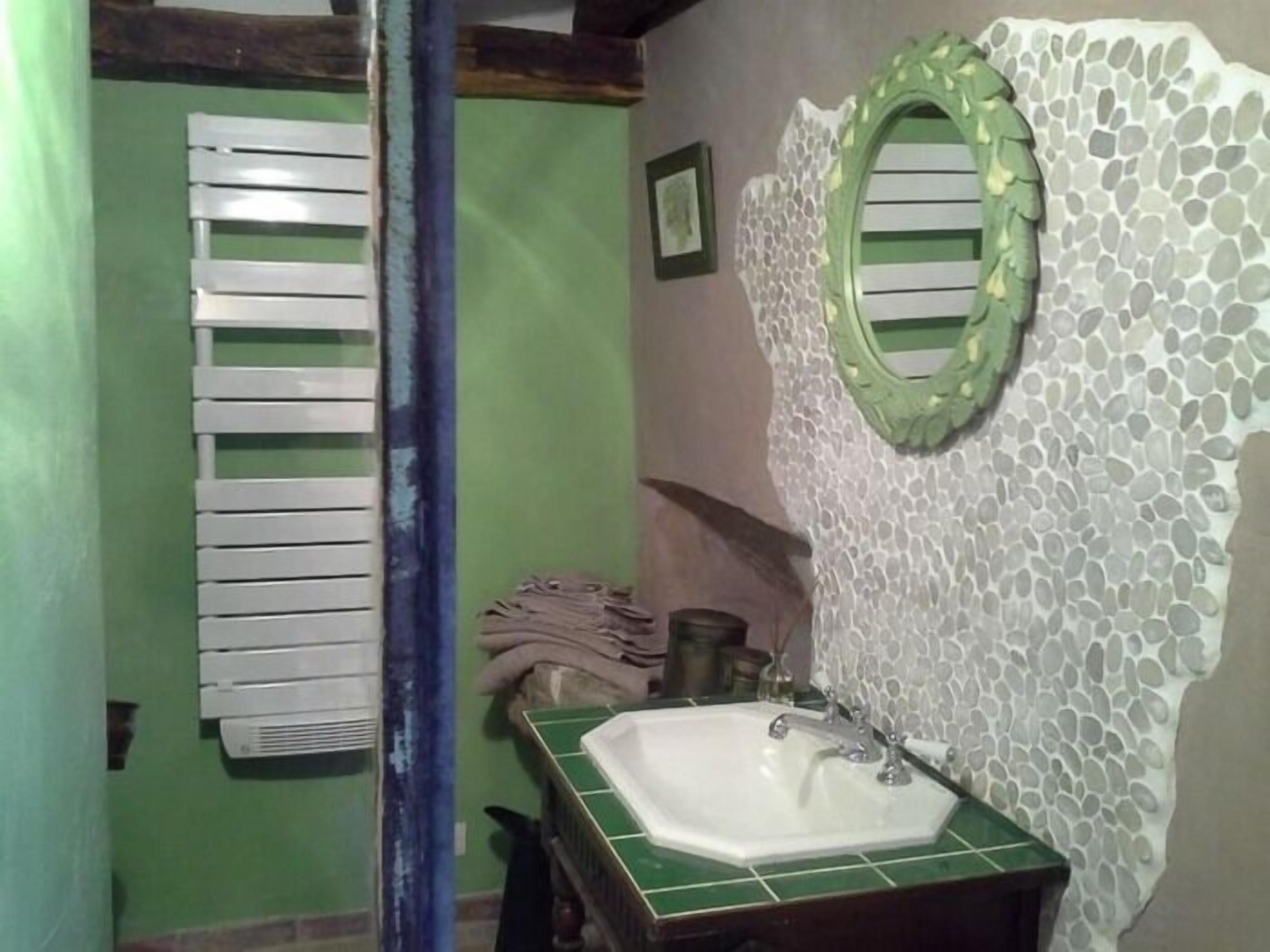 A bathroom with a green tiled sink, a white wall with a mosaic pattern, and a wooden door with a white towel rack.