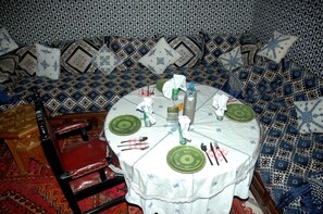 A dining area with a round table set for four, surrounded by patterned cushions and a red leather chair.