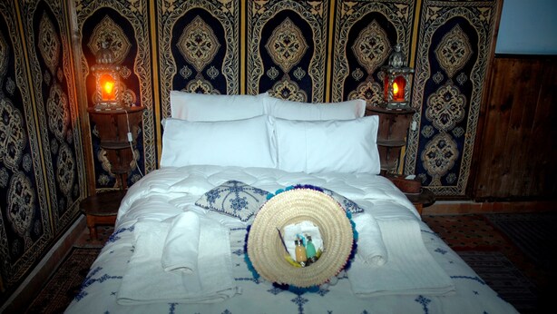A bed with white linens and a decorative headboard with intricate patterns. - Riad Lahboul (Meknes)