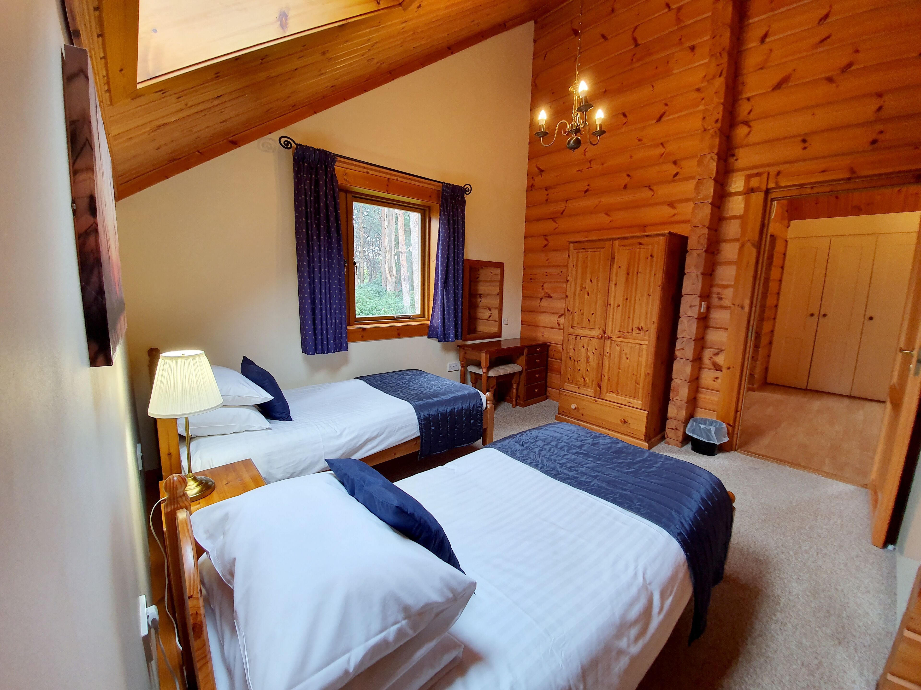 A log cabin-style room with two beds, a desk, and a wardrobe.