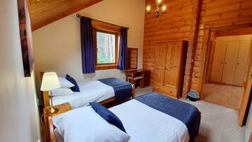 A log cabin-style room with two beds, a desk, and a wardrobe.