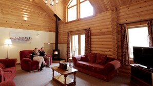 A log cabin interior with a fireplace, red furniture, and a television. - The Dorset Resort (Wareham)
