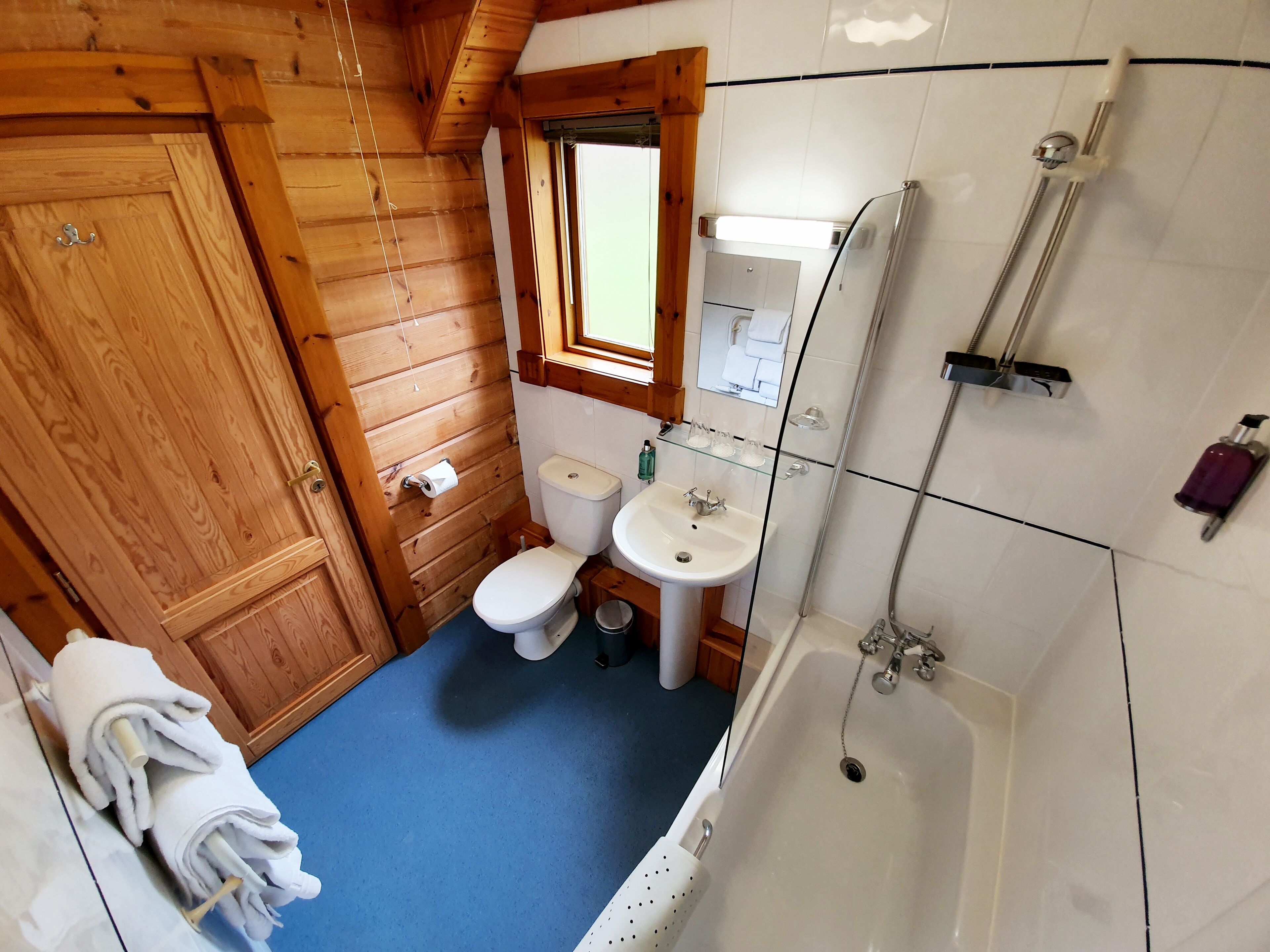 A wooden cabin bathroom with a toilet, sink, and shower.