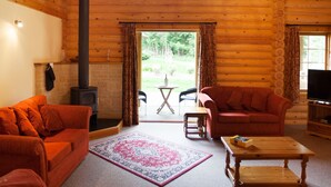 A log cabin interior with a fireplace, two sofas, a television, and a large window. - The Dorset Resort (Wareham)