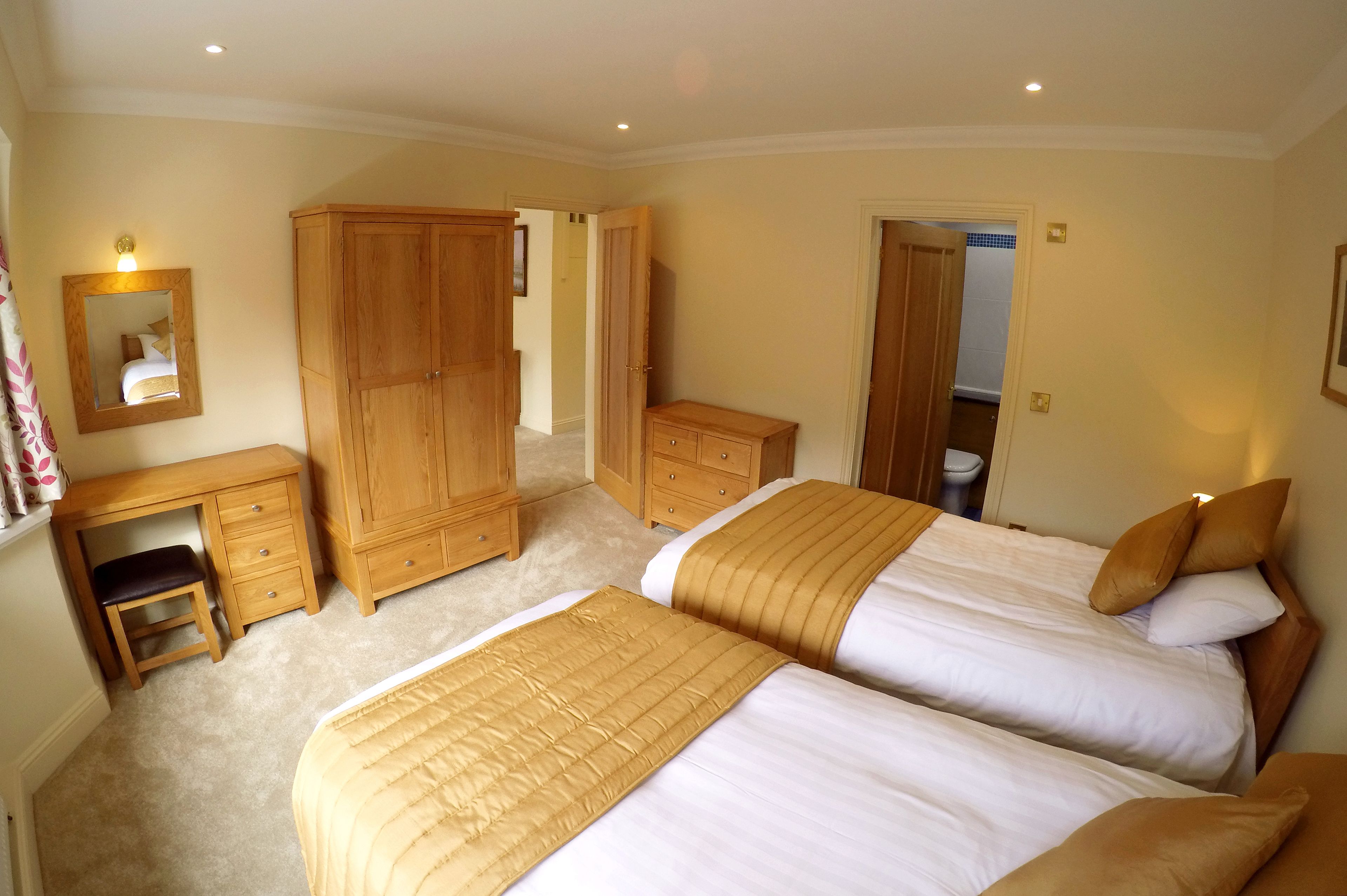 A bedroom with two beds, a wooden wardrobe, a desk, and a mirror.