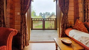 A cozy cabin room with a wooden floor, a bed with a white comforter, a wooden table with a scale, and curtains. - The Dorset Resort (Wareham)