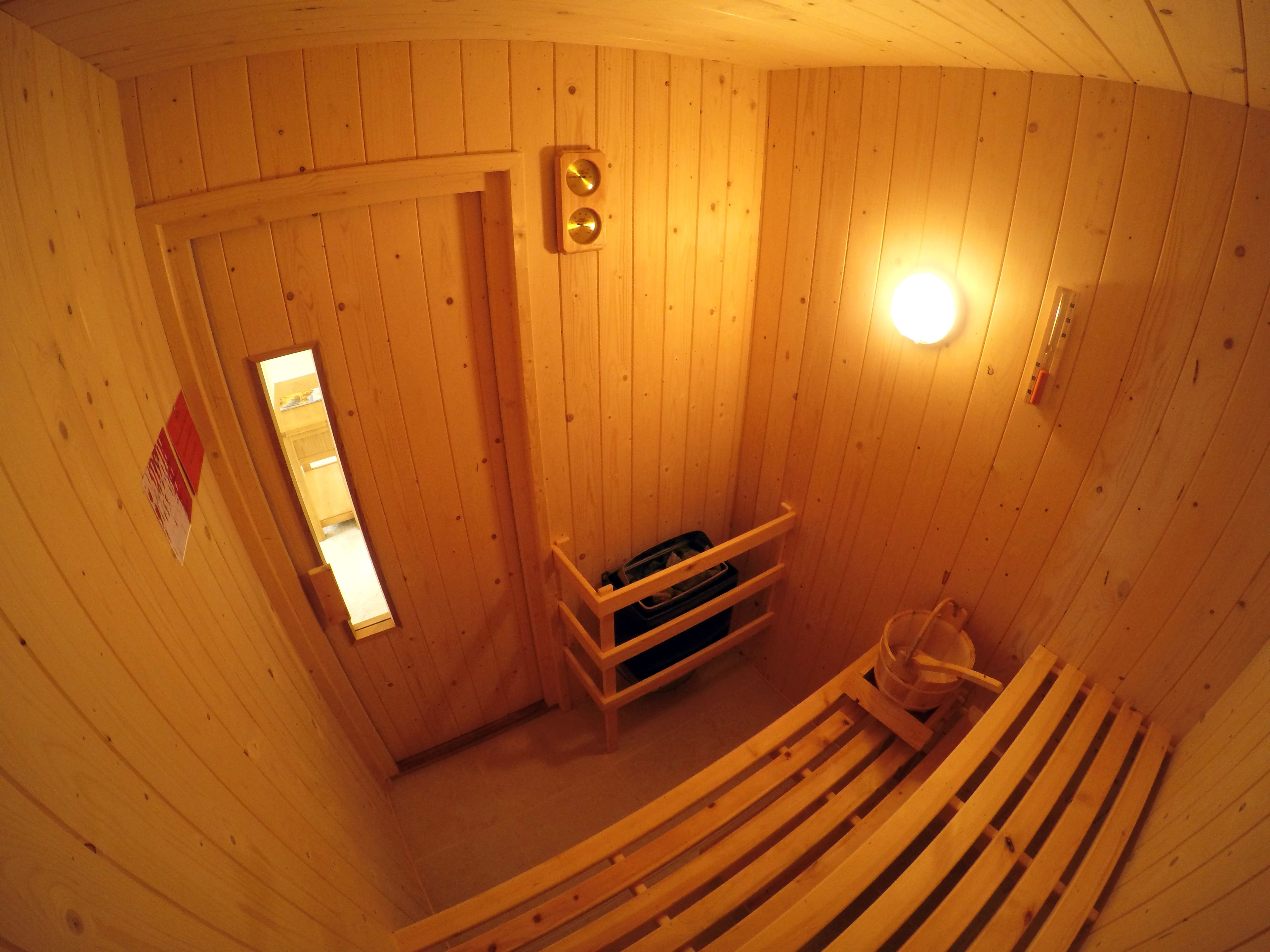 En bastu gjord av trä, med en bänk, en bänk med en handduk på och en dörr med ett fönster.